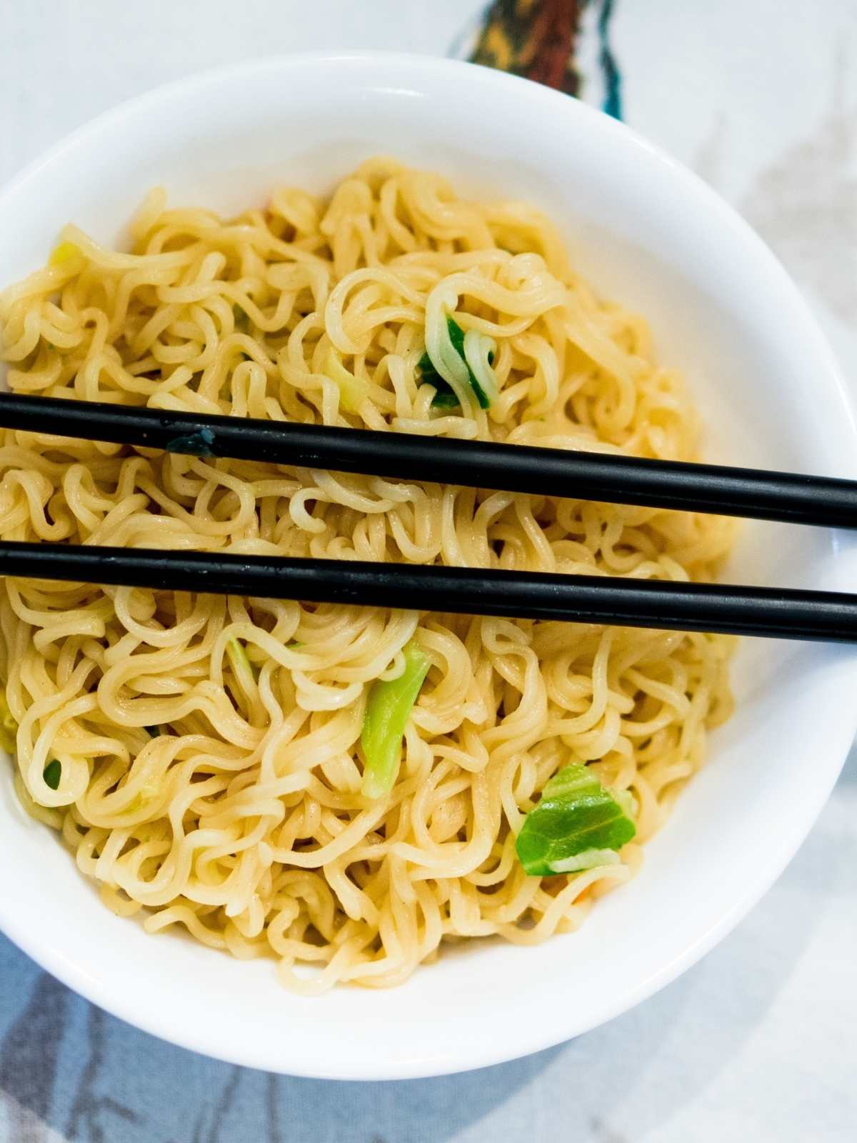 White bowl filled with ramen with chopsticks laying across the top.