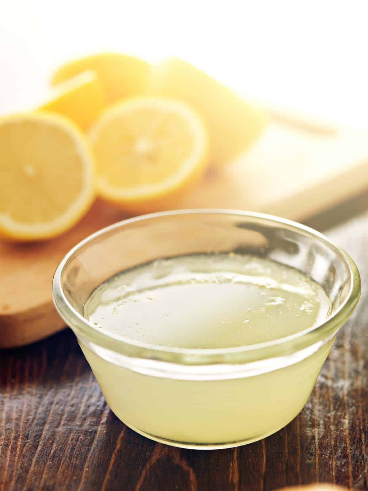 Lemon juice in a glass jar with sliced lemons behind it.