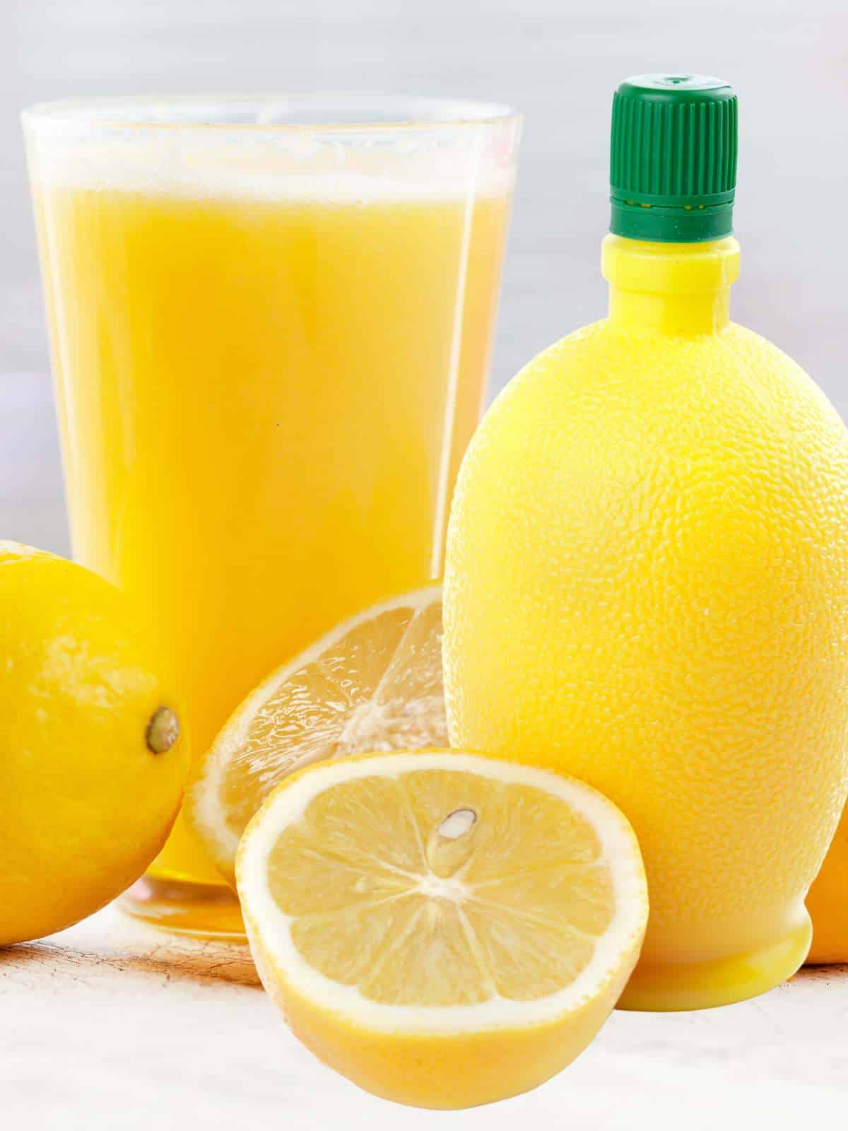 Bottled lemon juice next to a glass of fresh lemon juice with sliced lemons.