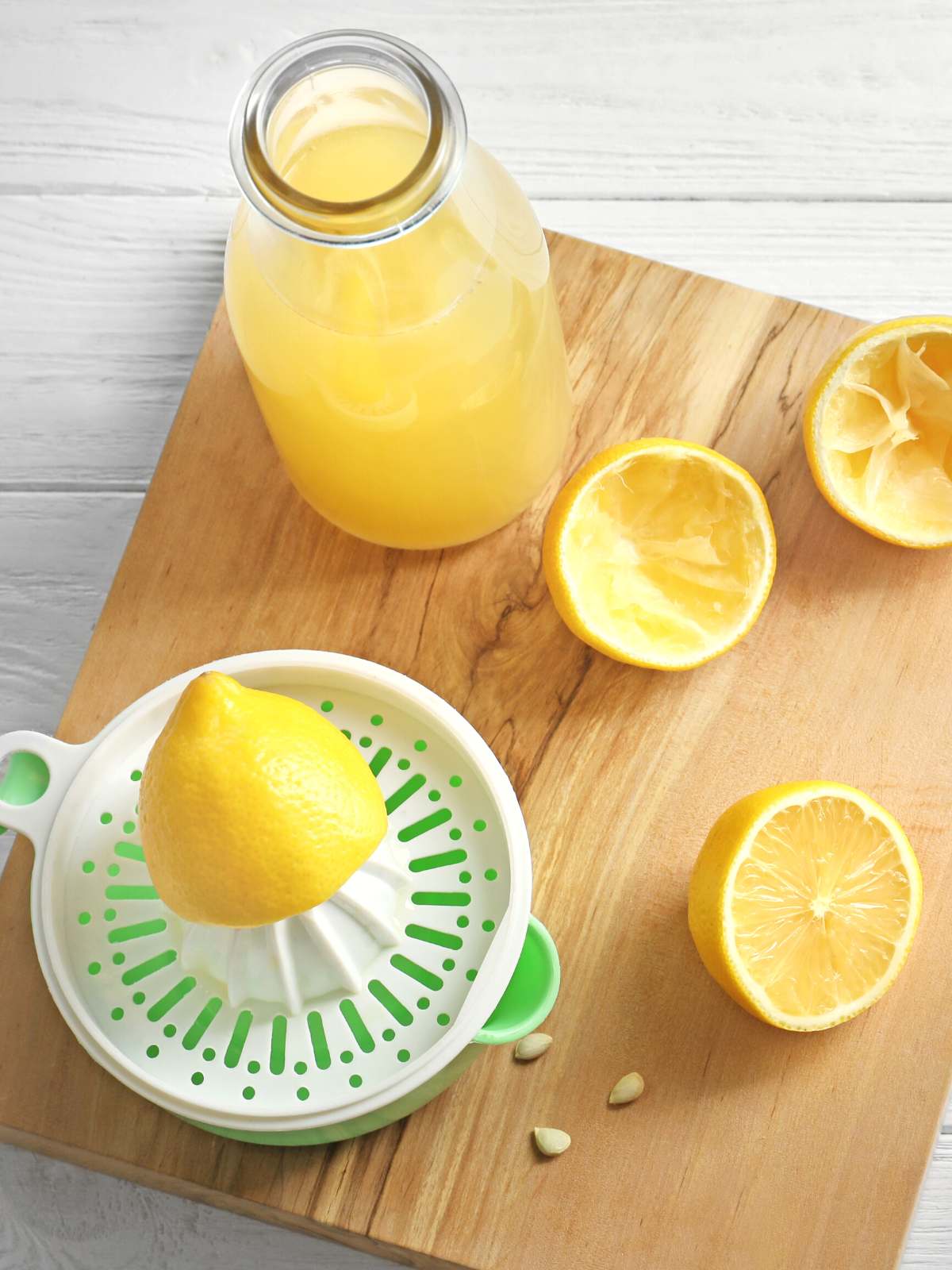 Lemons on a wooden cutting board with a citrus juicer and a glass of lemon juice.