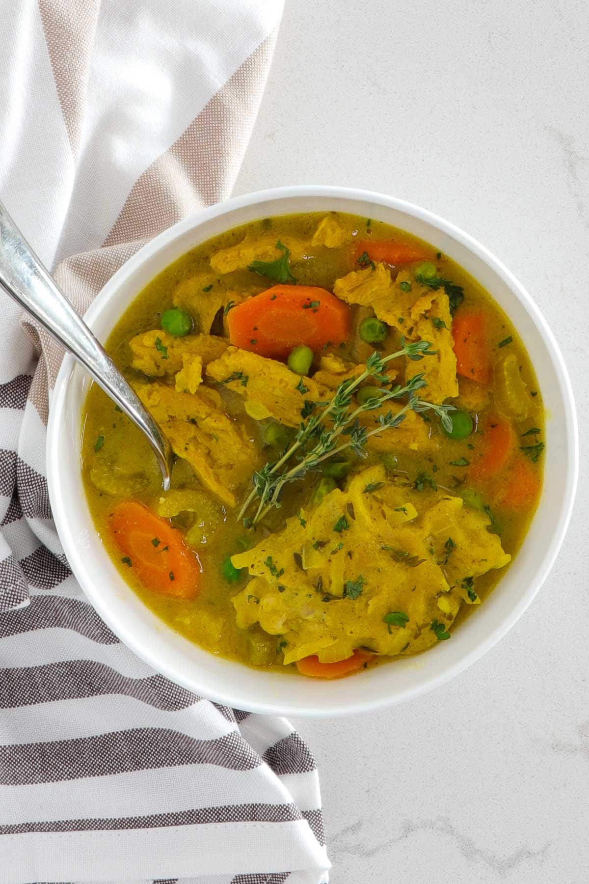 A bowl of vegan chicken and dumpling stew with a spoon and a cloth napkin beside it.