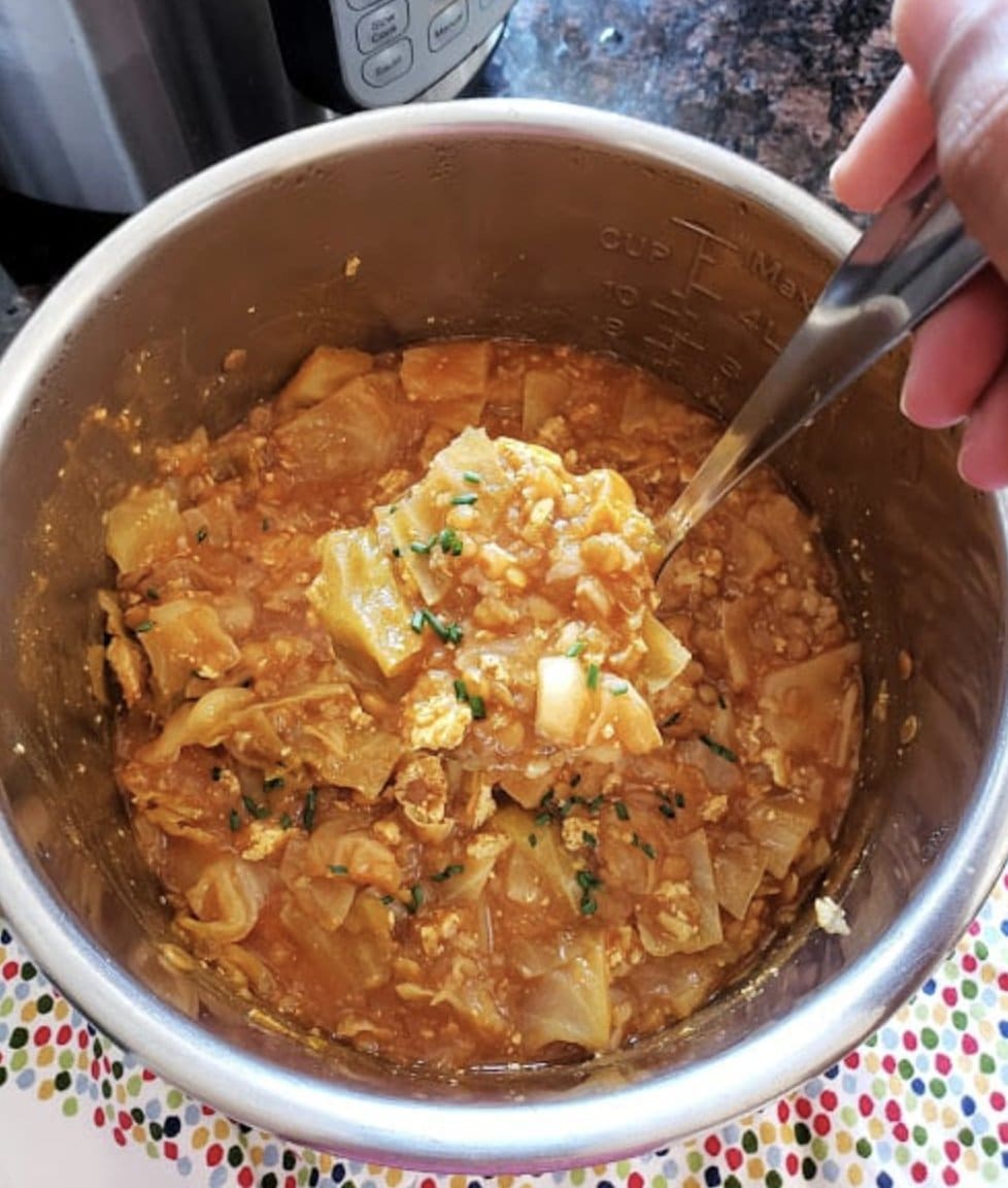 Cabbage stew in a pot with a hand holding a ladle and scooping some up.