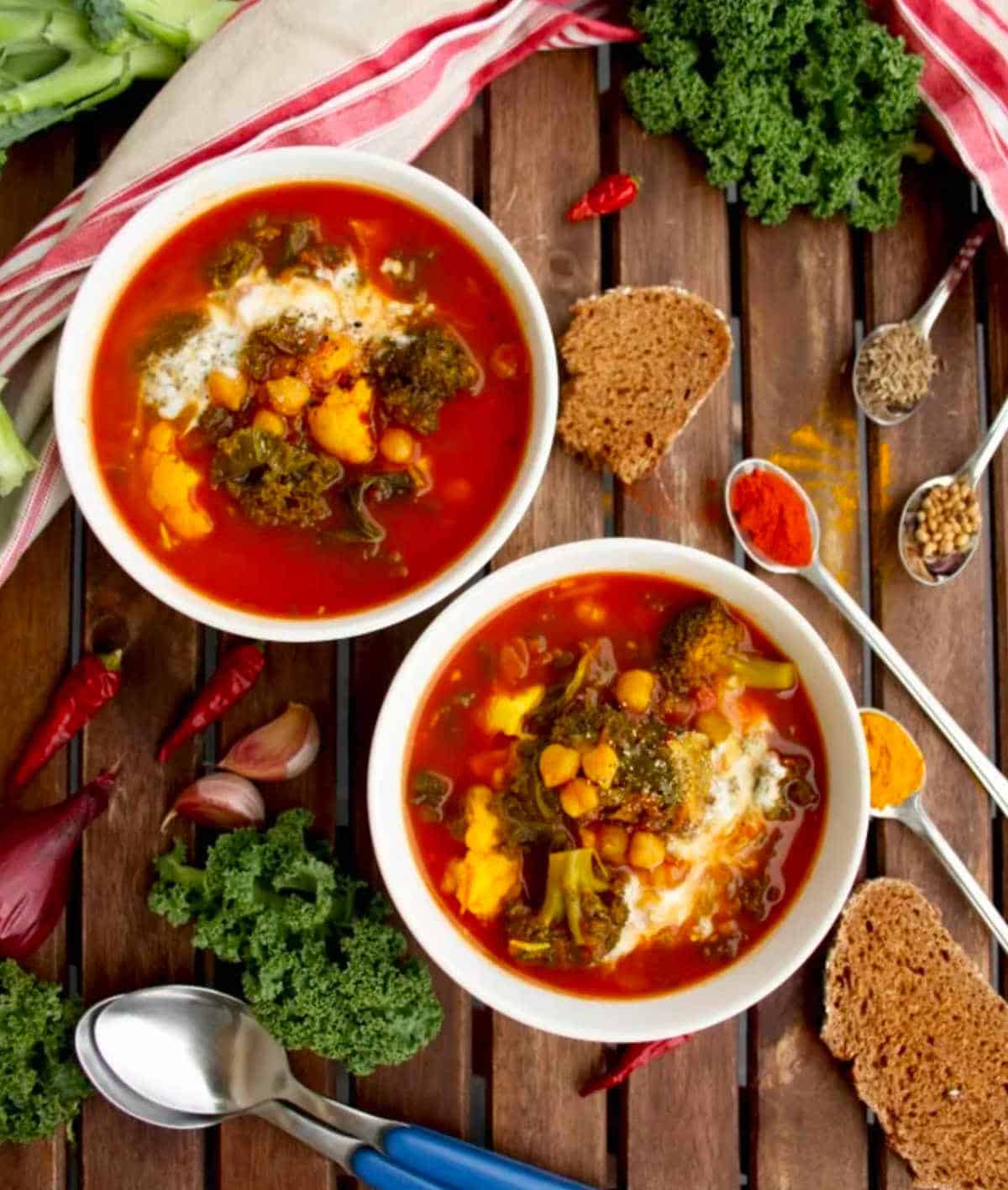 Two bowls of vegan cauliflower stews with a couple spoons and various ingredients surrounding them.