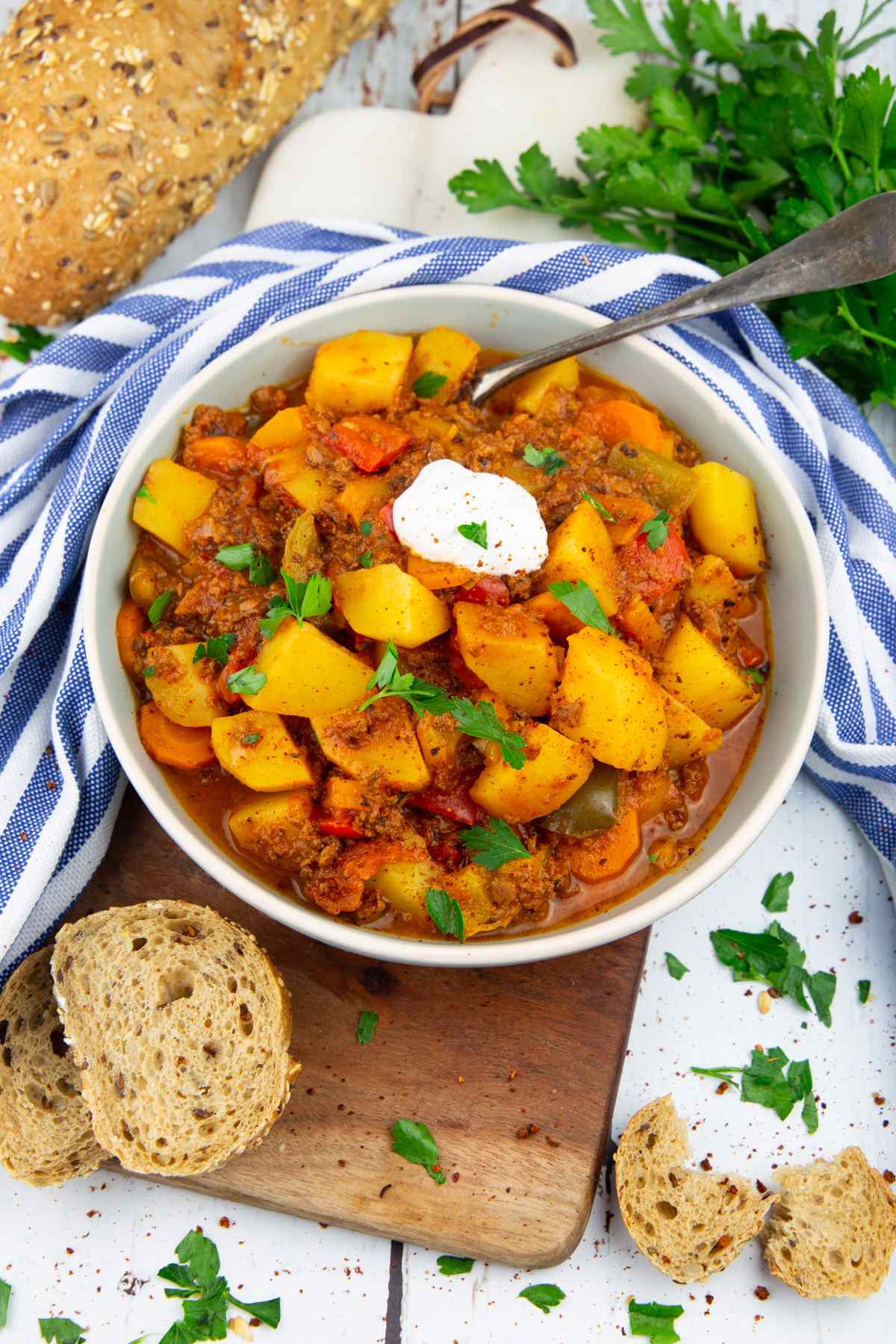 Bowl of potato stew with a spoon, cloth napkin, and slice of bread.