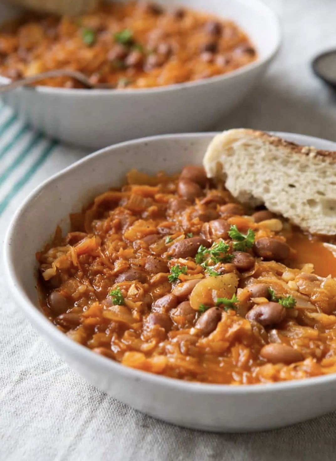 Two bowls filled with sauerkraut bean stew and serve with a slice of crusty bread.