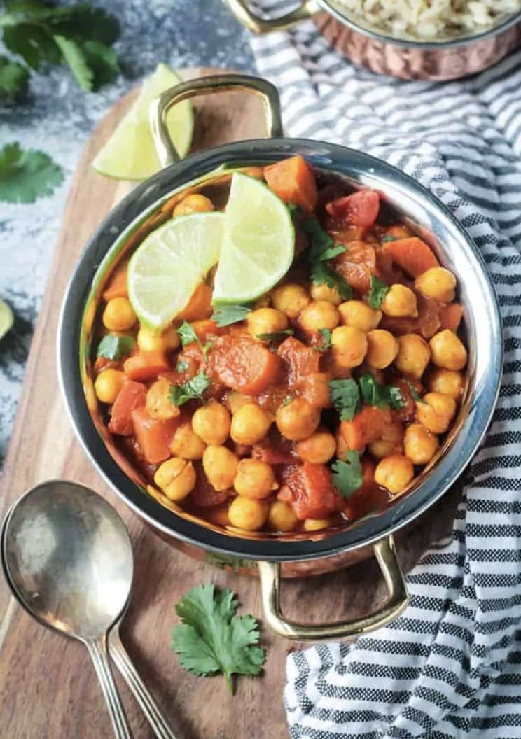 Bowl of spiced chickpea stew serve with lime slice and cilantro on top.