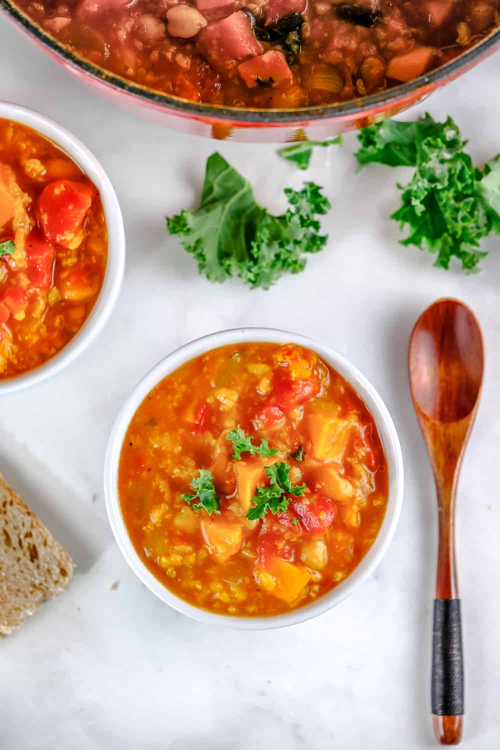 Sweet potato stew in bowls with fresh kale and a spoon nearby.