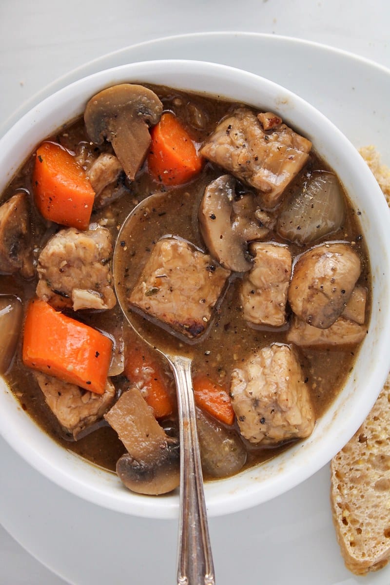 Vegan tempeh "beef" stew in a bowl with a spoon.