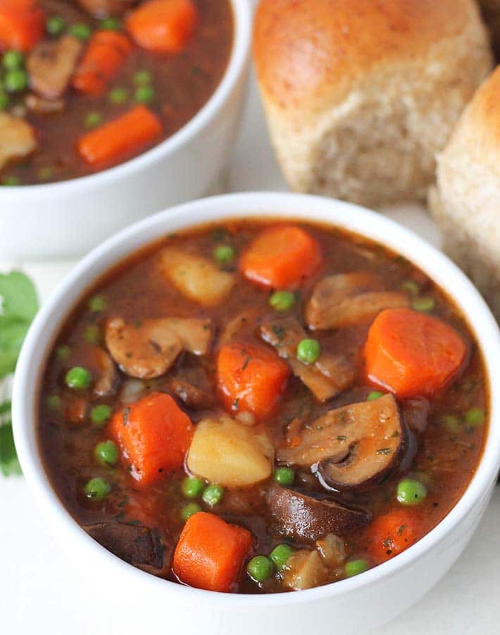 Chunky vegan stew served in a couple bowls with a dinner roll on the side.