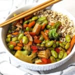 Stir fried vegetables and rice coated with vegan stir fry sauce in a bowl with chopsticks.