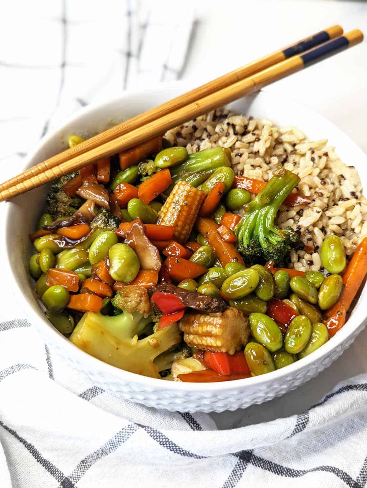 Stir fried vegetables and rice coated with vegan stir fry sauce in a bowl with chopsticks.