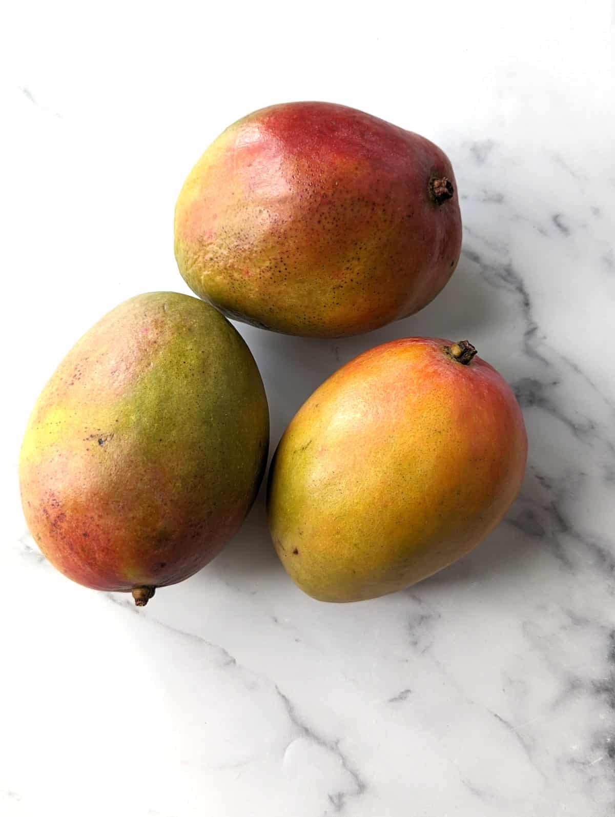 Three ripe mangos on a marble counterop.