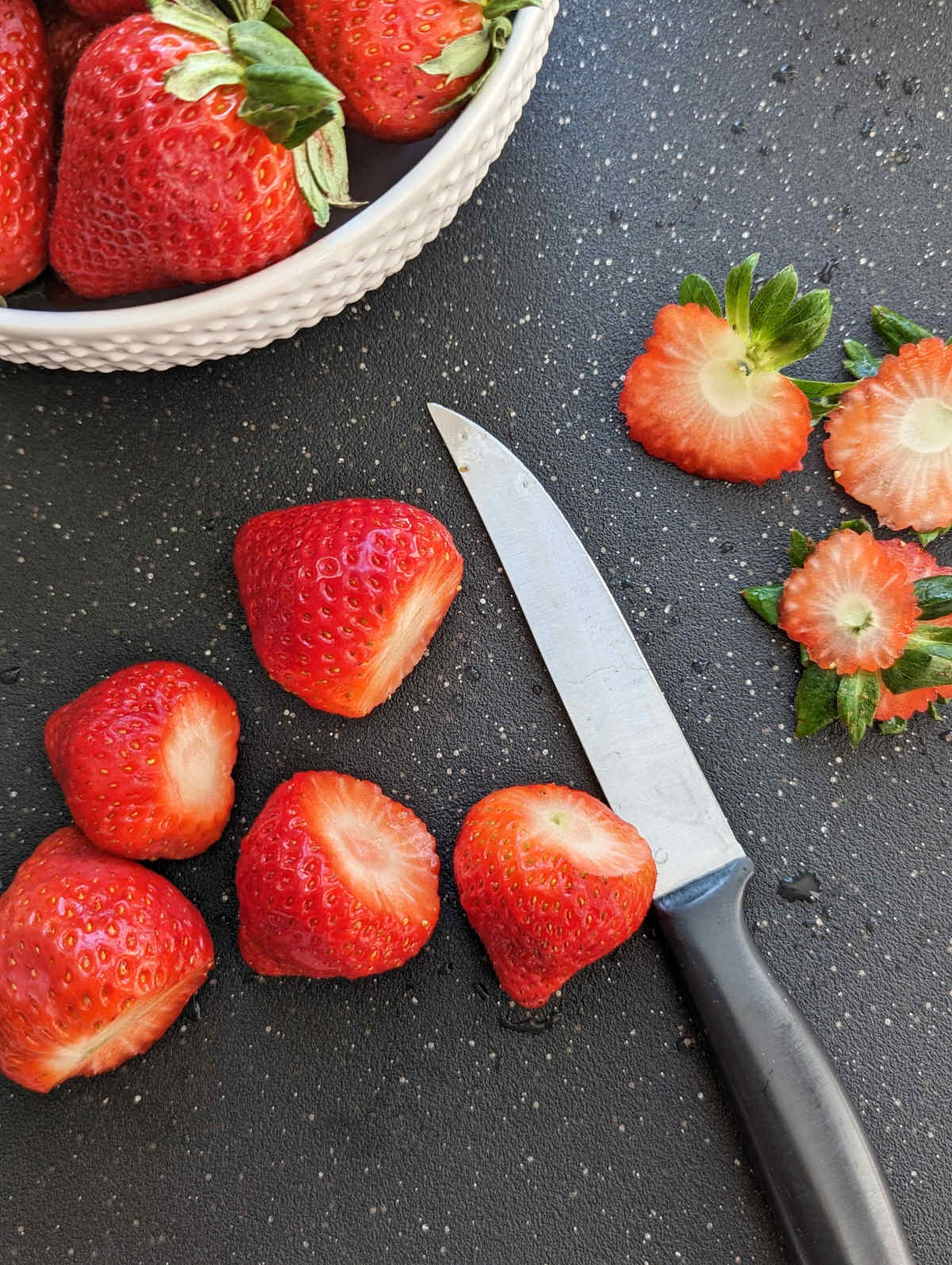 Strawberries with the tops sliced off next to a knife on a cutting board.