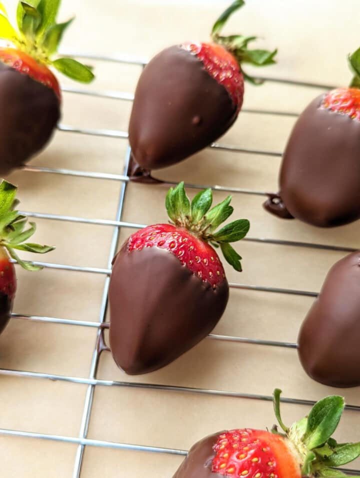 Chocolate covered strawberries drying on a rack placed over parchment paper.