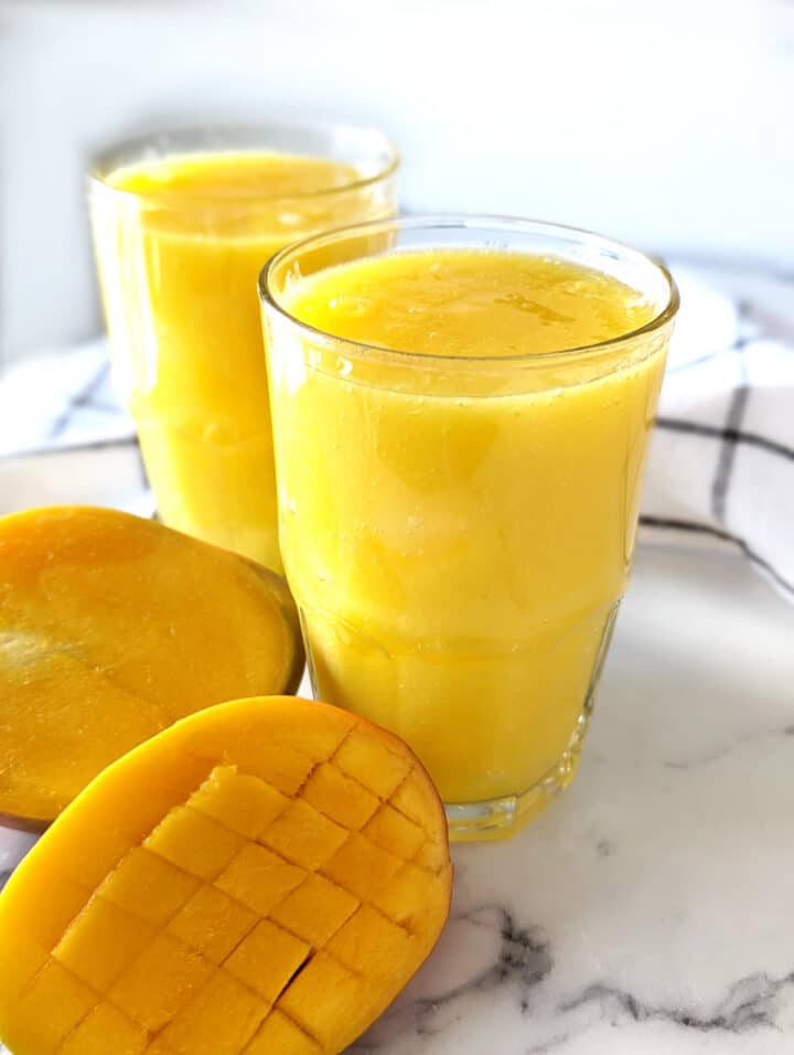 Two glasses of mango juice with sliced mango next to the glasses.