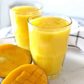Two glasses of mango juice with sliced mango next to the glasses.