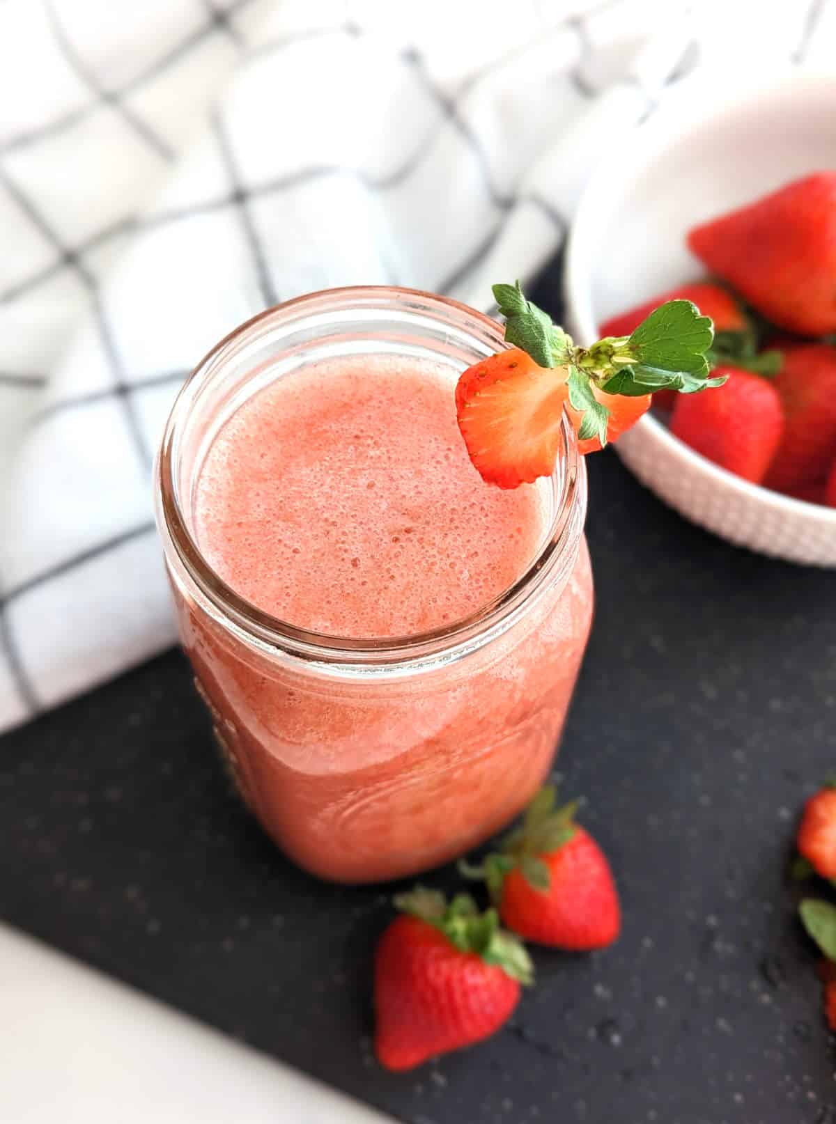 Strawberry juice in a mason jar with a slice of strawberry on the lip of the jar.