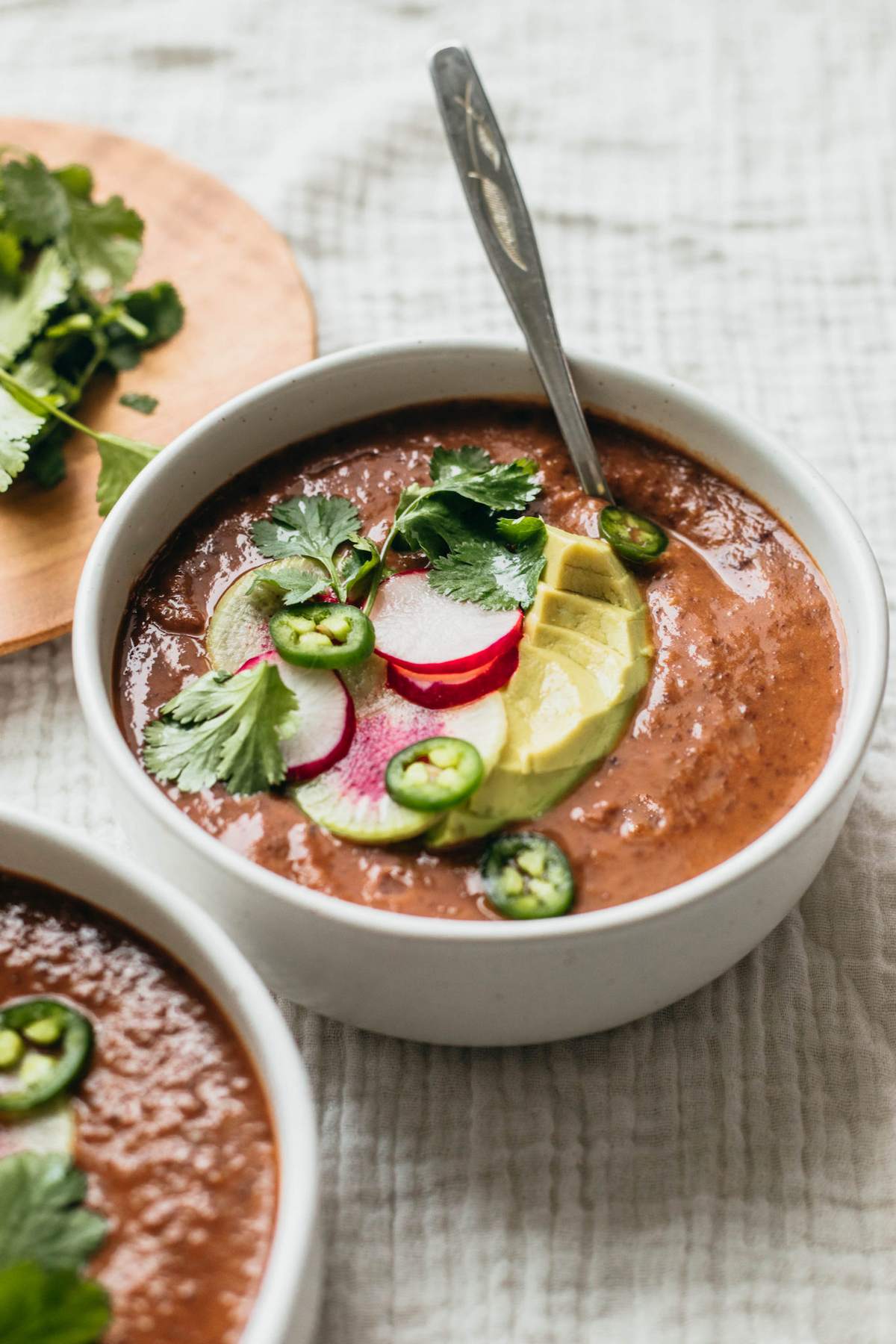 Bowl of creamy black bean soup topped with sliced radish, avocado, and cilantro.