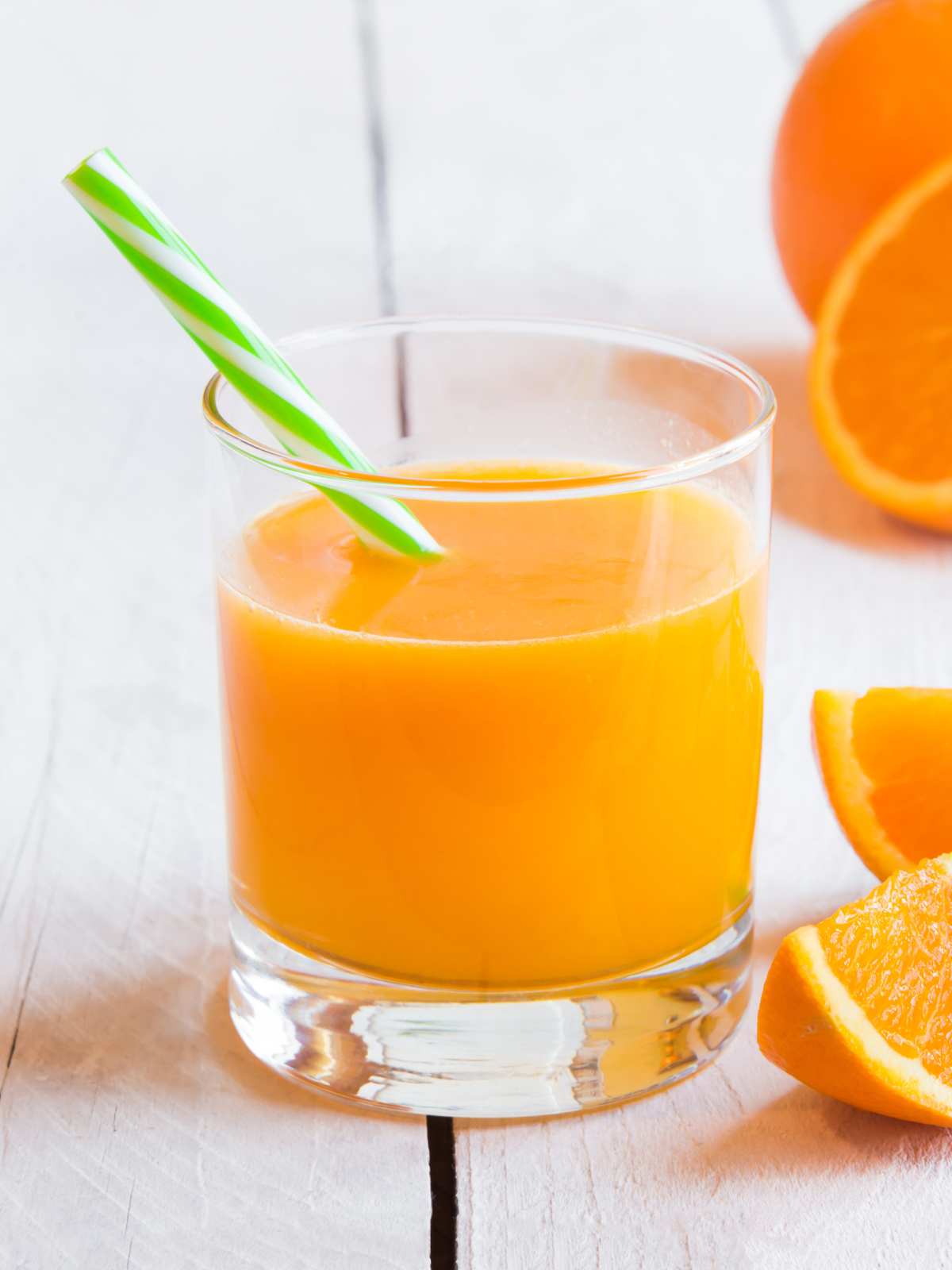 A glass of freshly made orange juice with a straw next to slices of oranges.