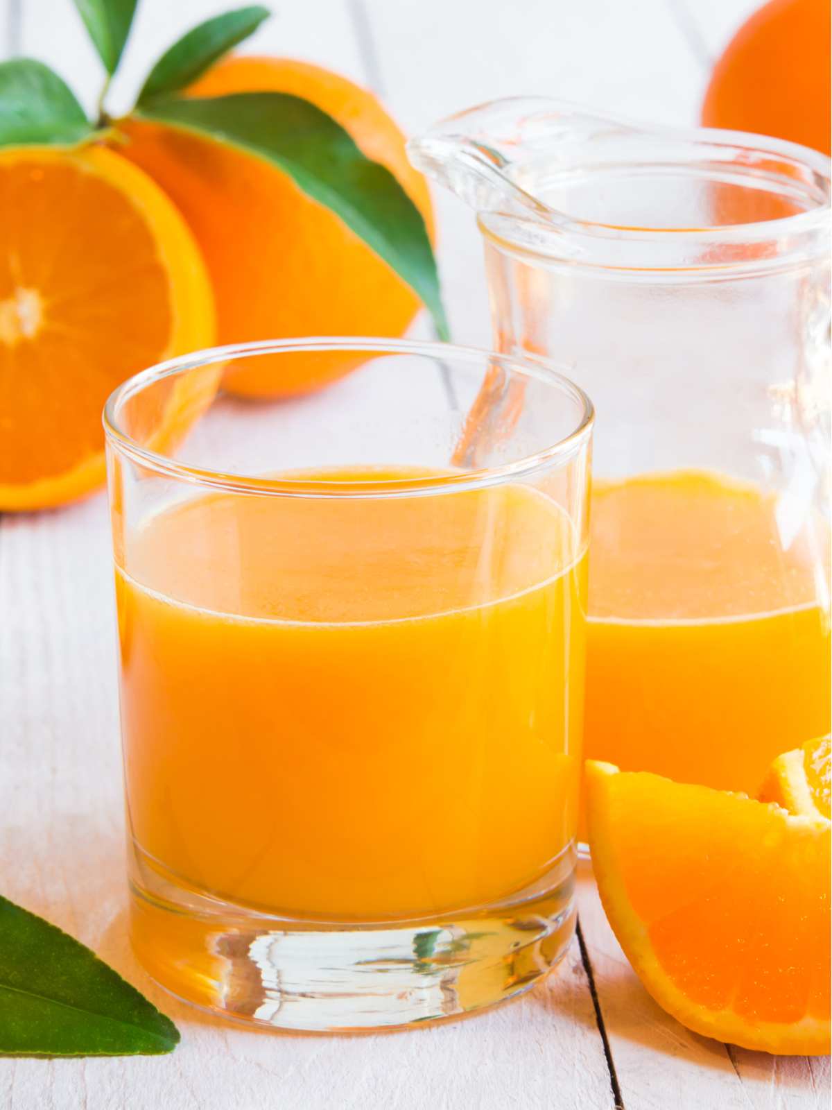 A glass of orange juice next to a pitcher of orange juice.