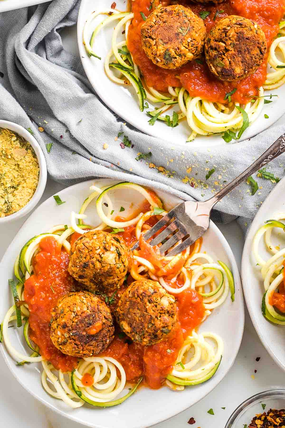 Two plates with zucchini noodles topped with red sauce and vegan meatballs.