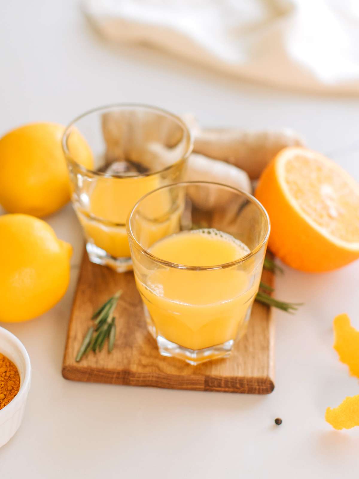 Two small glasses of ginger shots on a cutting board with various ingredients scattered around.