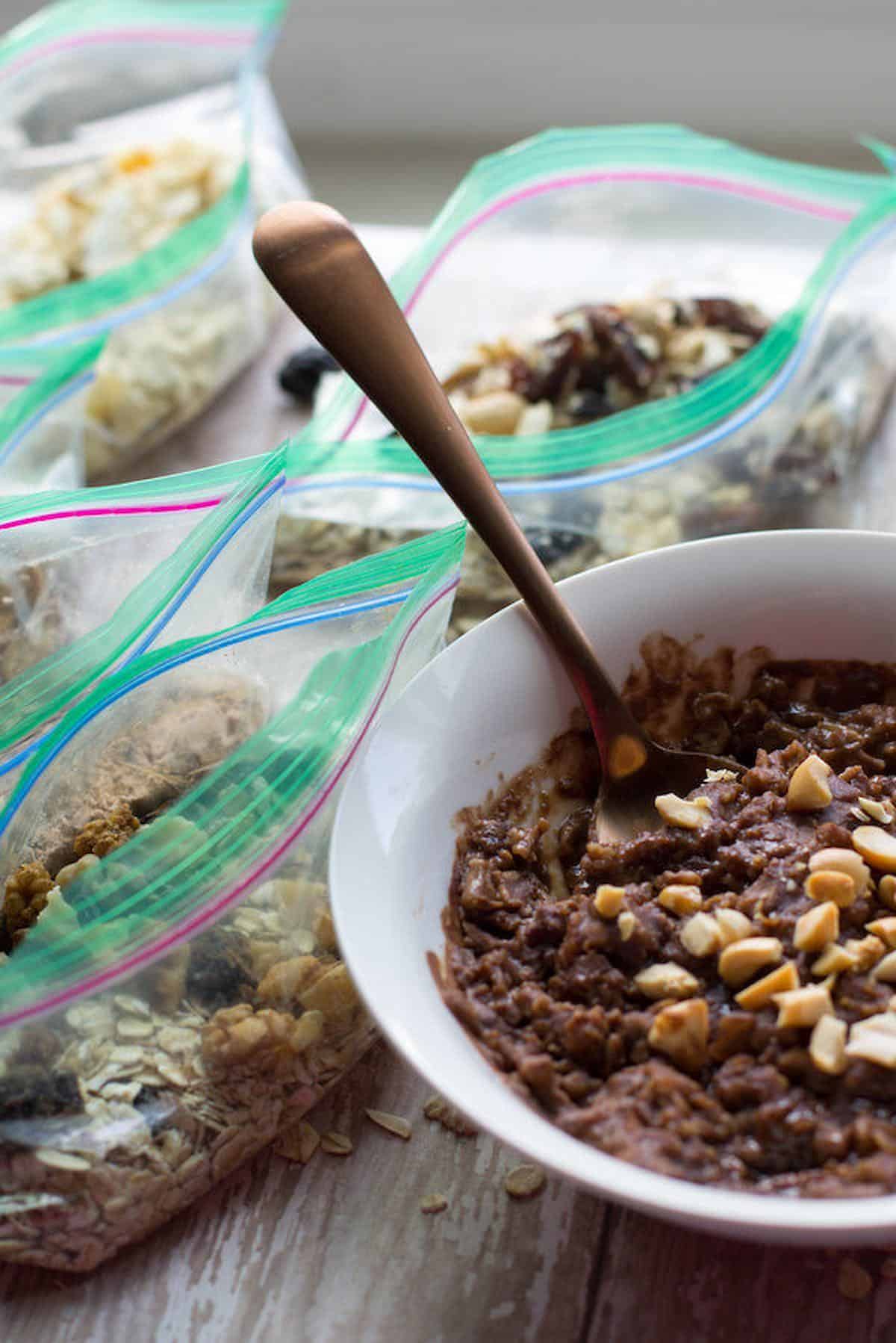 Bowl of oatmeal next to several plastic baggies of homemade oatmeal packets.