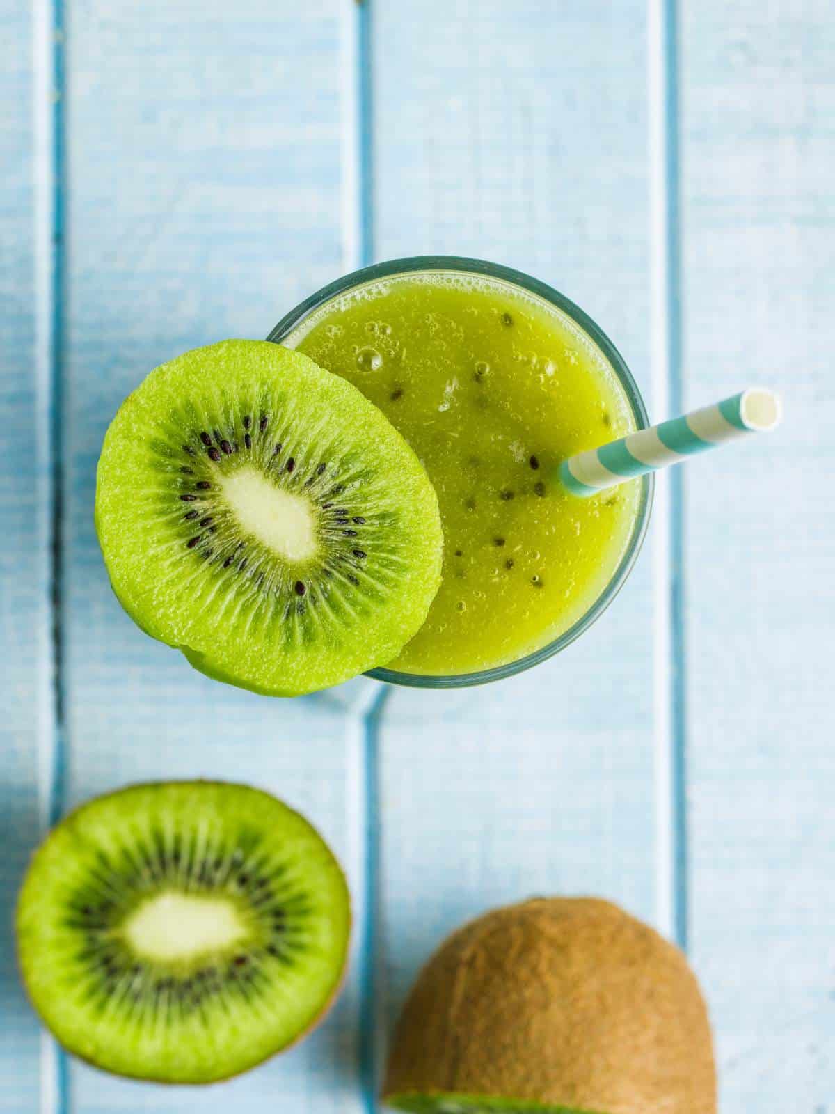 A glass of kiwi juice with a straw and a slice of kiwi sitting on the rim of the glass.