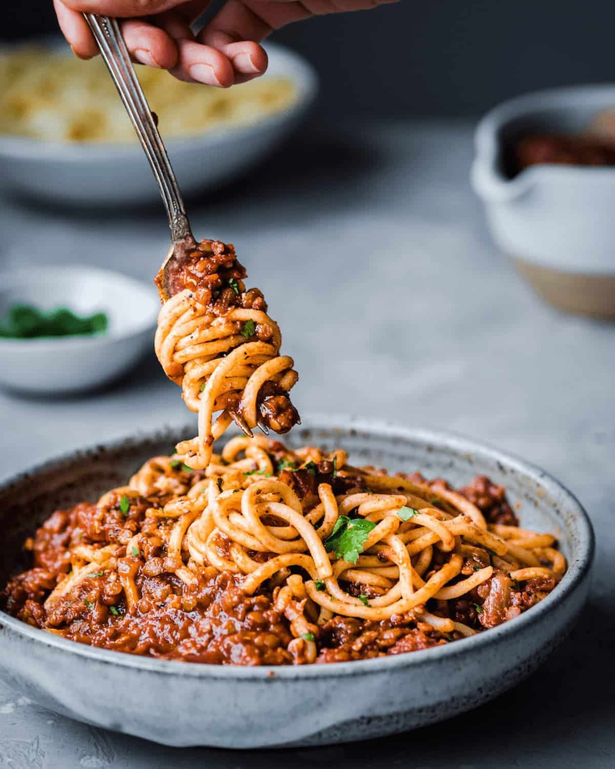 Bowl of red lentil bolognese past with a fork twirling a bite from it.