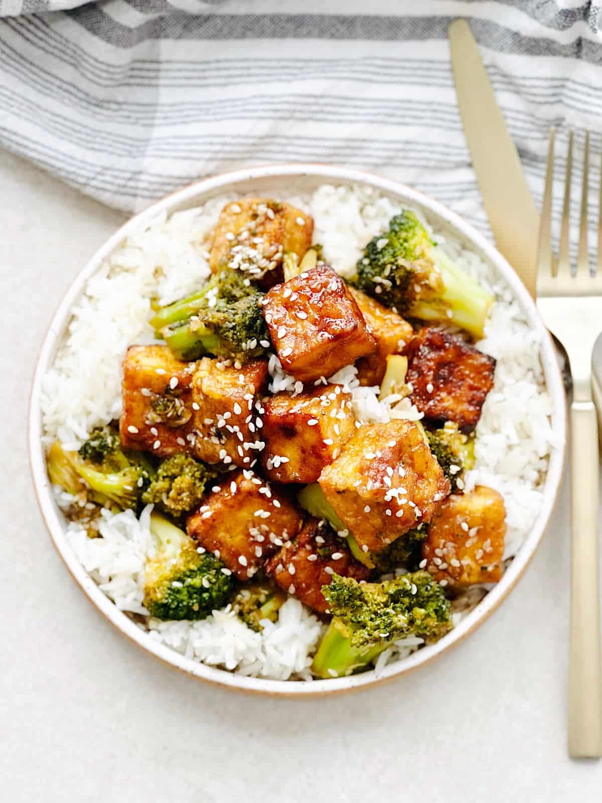 Bowl of rice topped with veggies and sticky tofu.