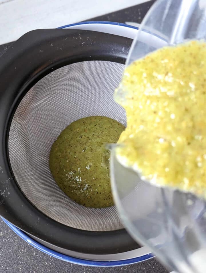 Pouring kiwi juice through a mesh strainer of a bowl.