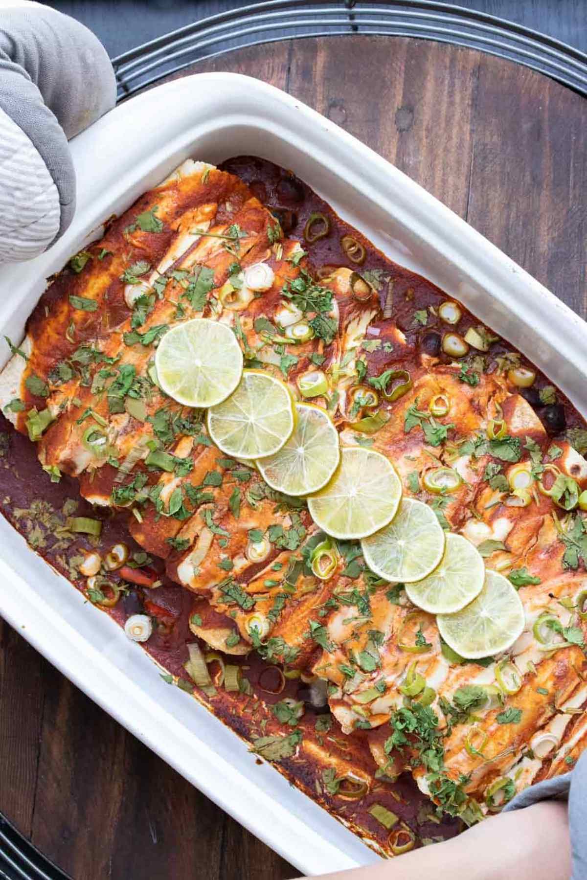 A casserole dish filled with black bean enchiladas topped with lime slices.