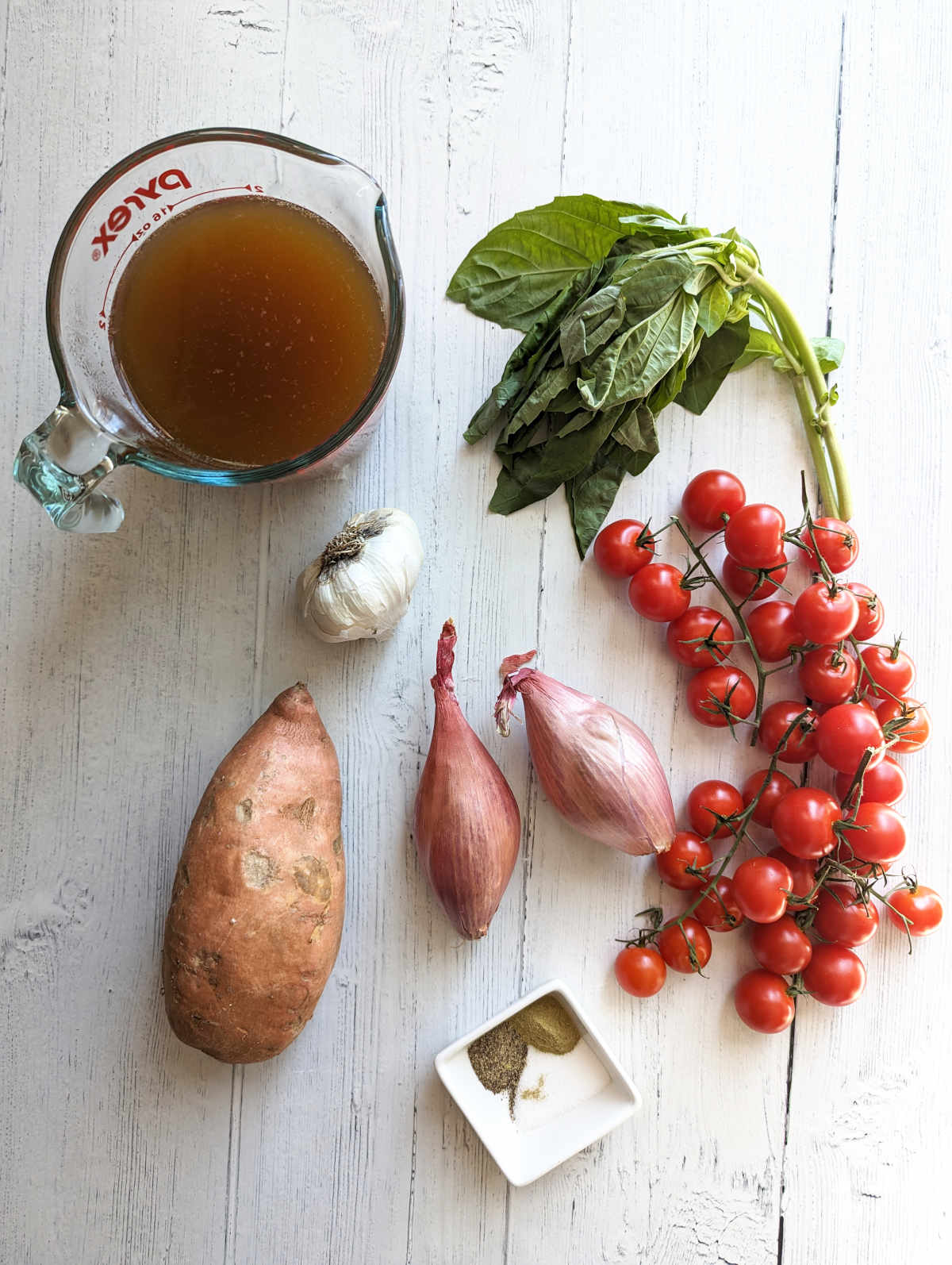 Ingredients for cherry tomato soup on a white wooden tabletop.