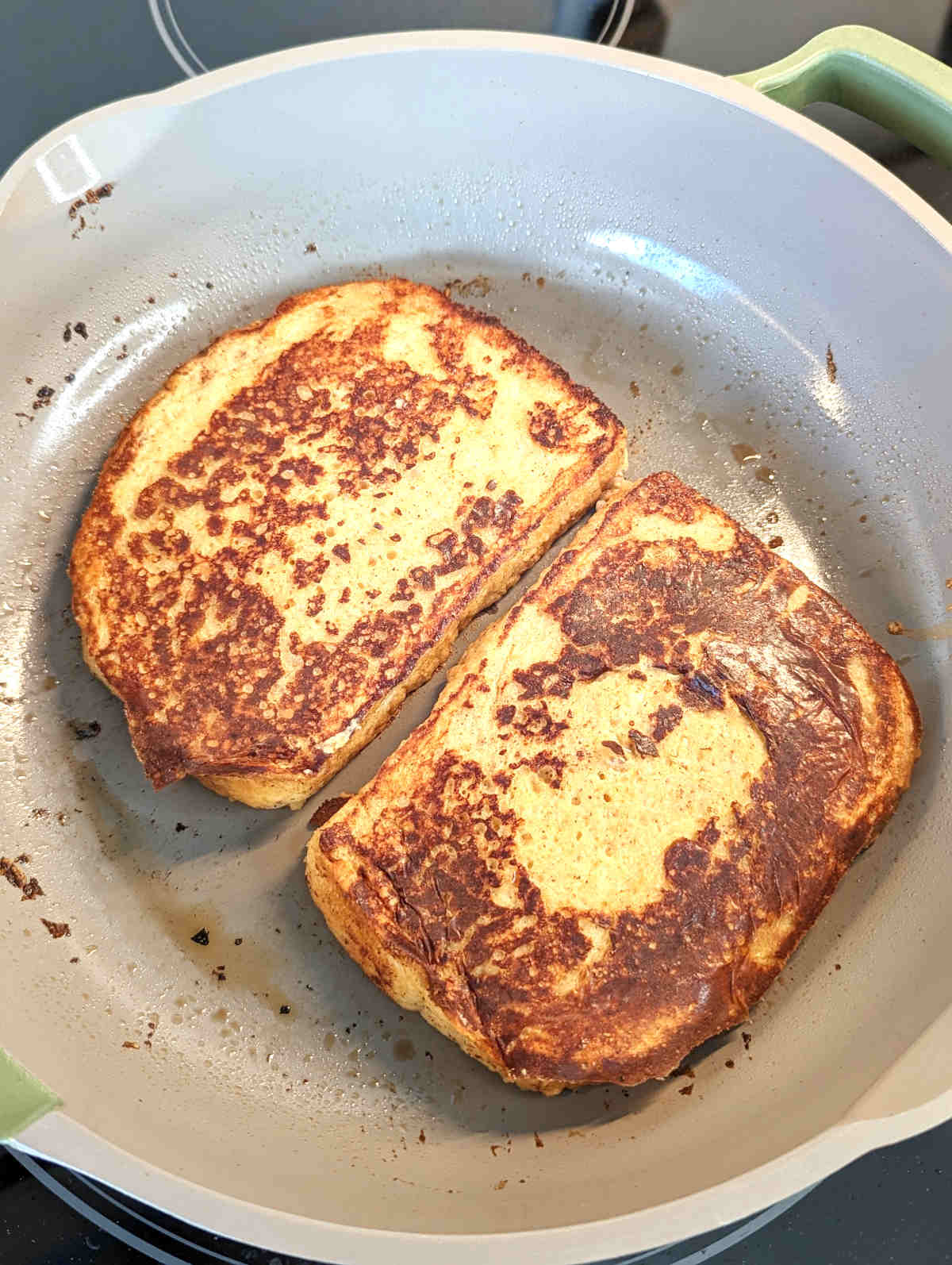 Two slices of vegan Just Egg french toast cooking in a skillet.