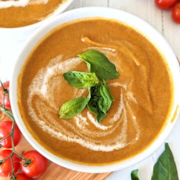 Roasted cherry tomato soup in a bowl with a swirl of coconut milk and topped with fresh basil leaves.