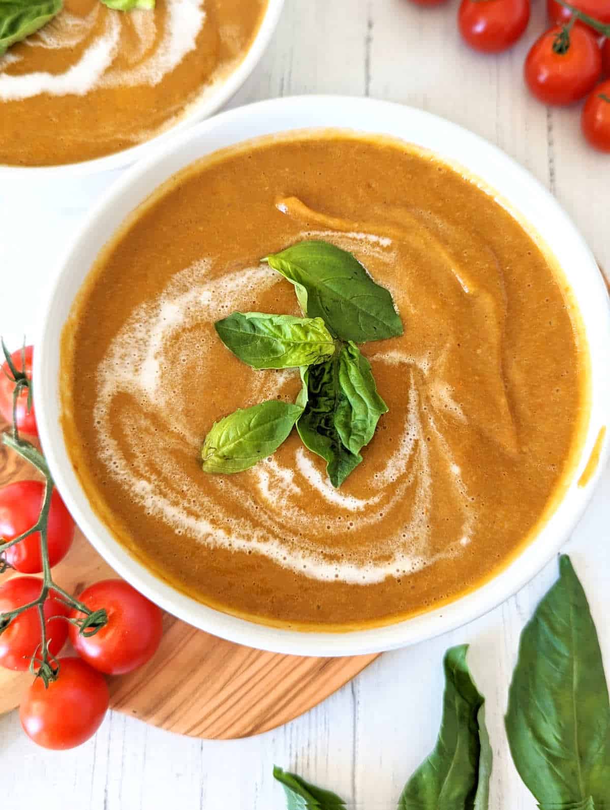 Roasted cherry tomato soup in a bowl with a swirl of coconut milk and topped with fresh basil leaves.