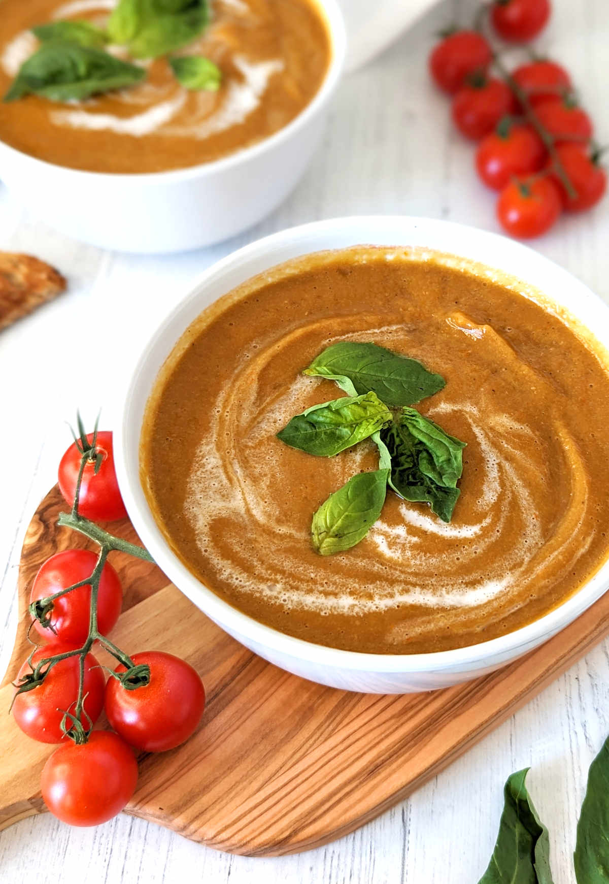 Roasted cherry tomato soup in a bowl with a swirl of coconut milk and topped with fresh basil leaves.