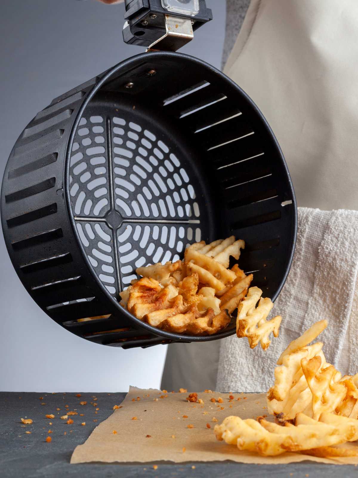 Someone holding an air fryer basket that's tilted over the counter with waffle fries falling out.