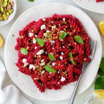 Beet pasta served in a white plate and topped with crumbled vegan feta, basil leaves, and crushed pistachios.
