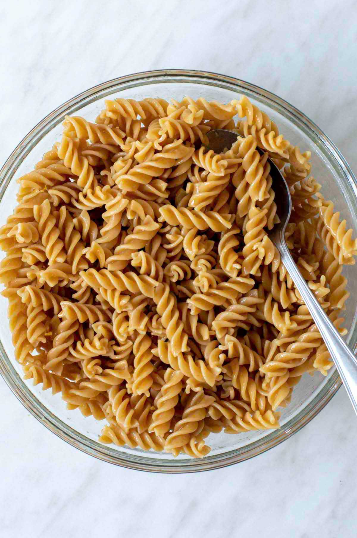 Cooked whole wheat fusilli coated with olive oil in a glass bowl.