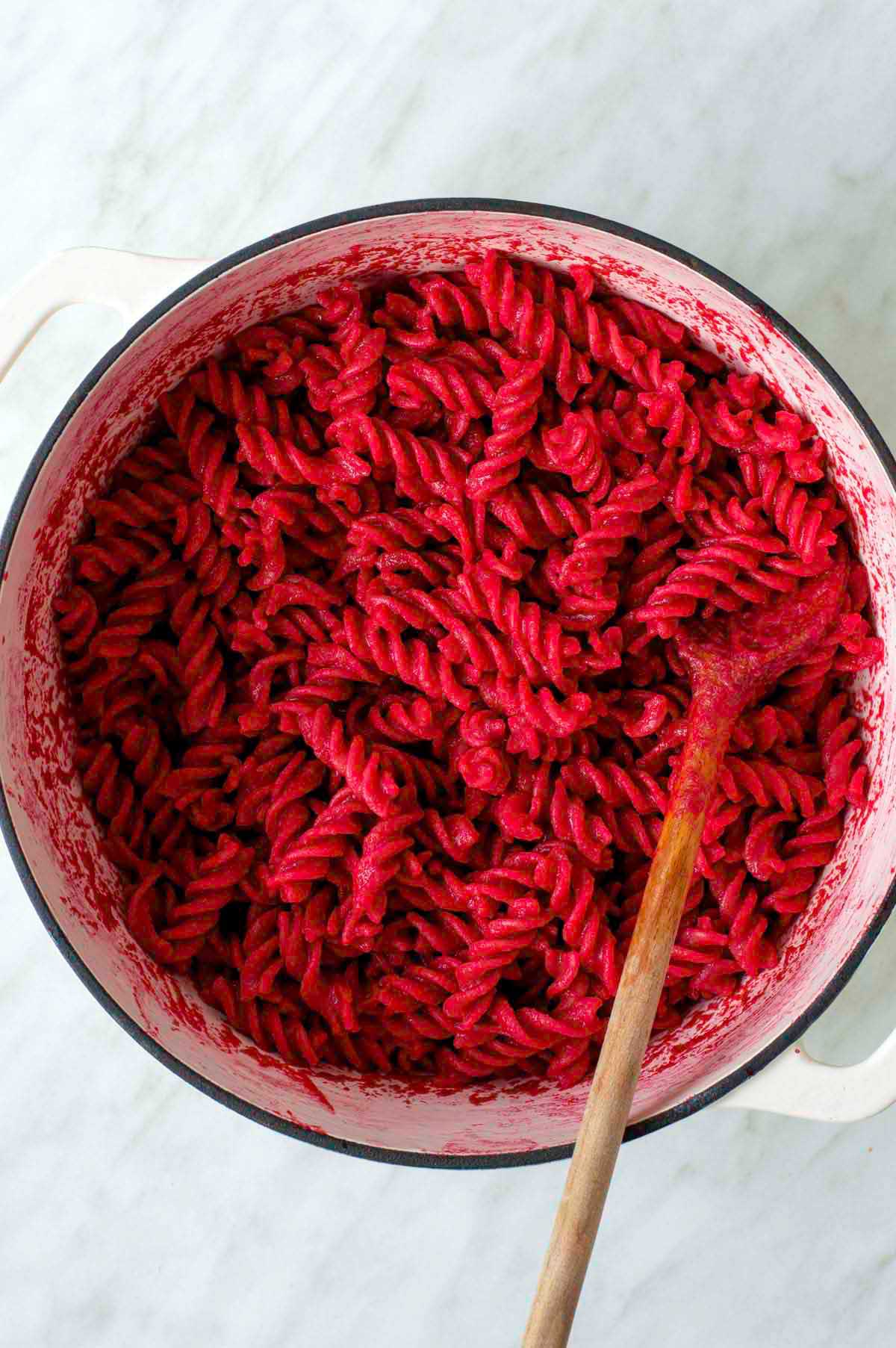 Beet pasta in a white Dutch oven with a wooden spoon dug in it.