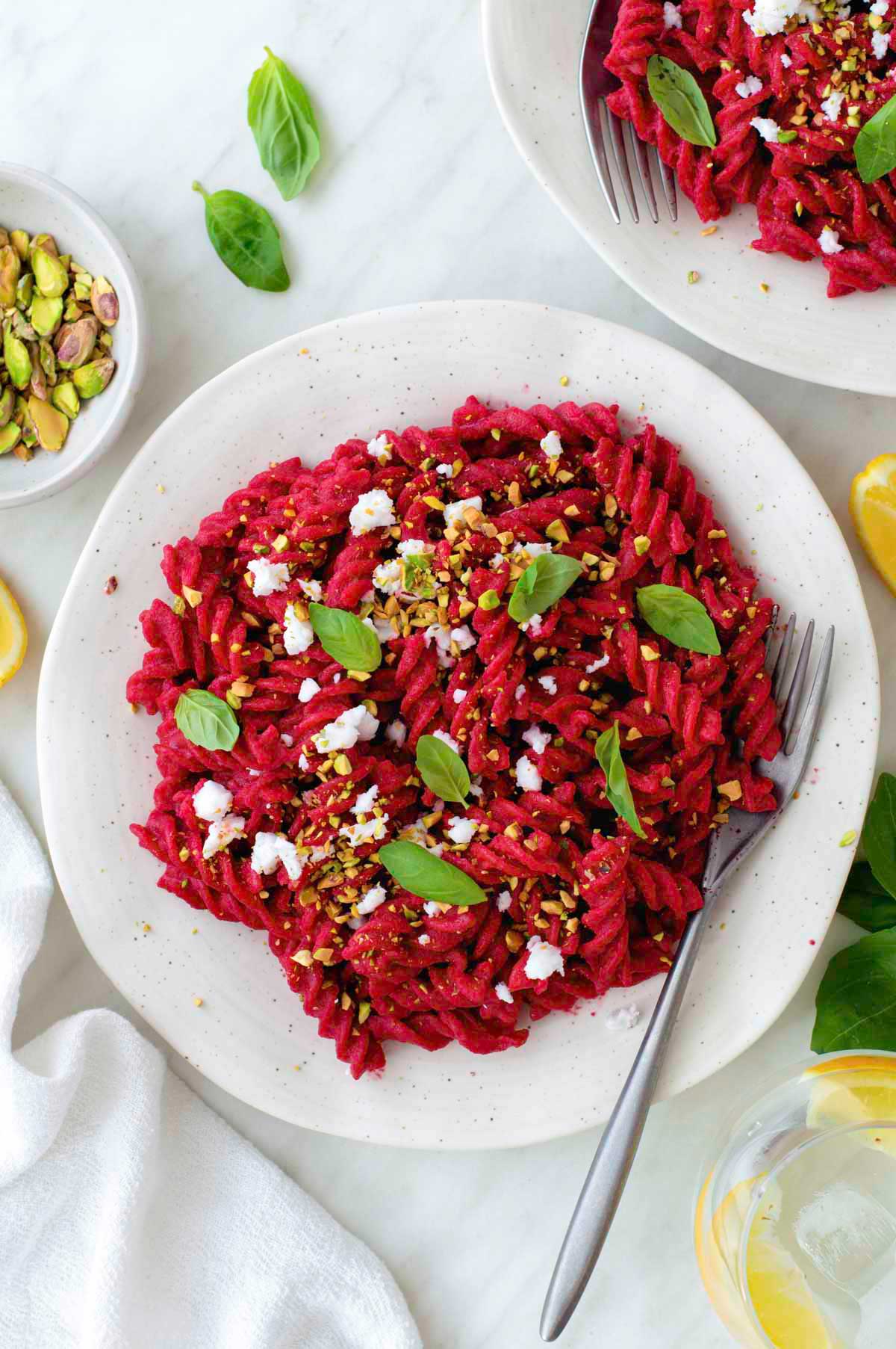 Beet pasta served in a white plate and topped with crumbled vegan feta, basil leaves, and crushed pistachios.