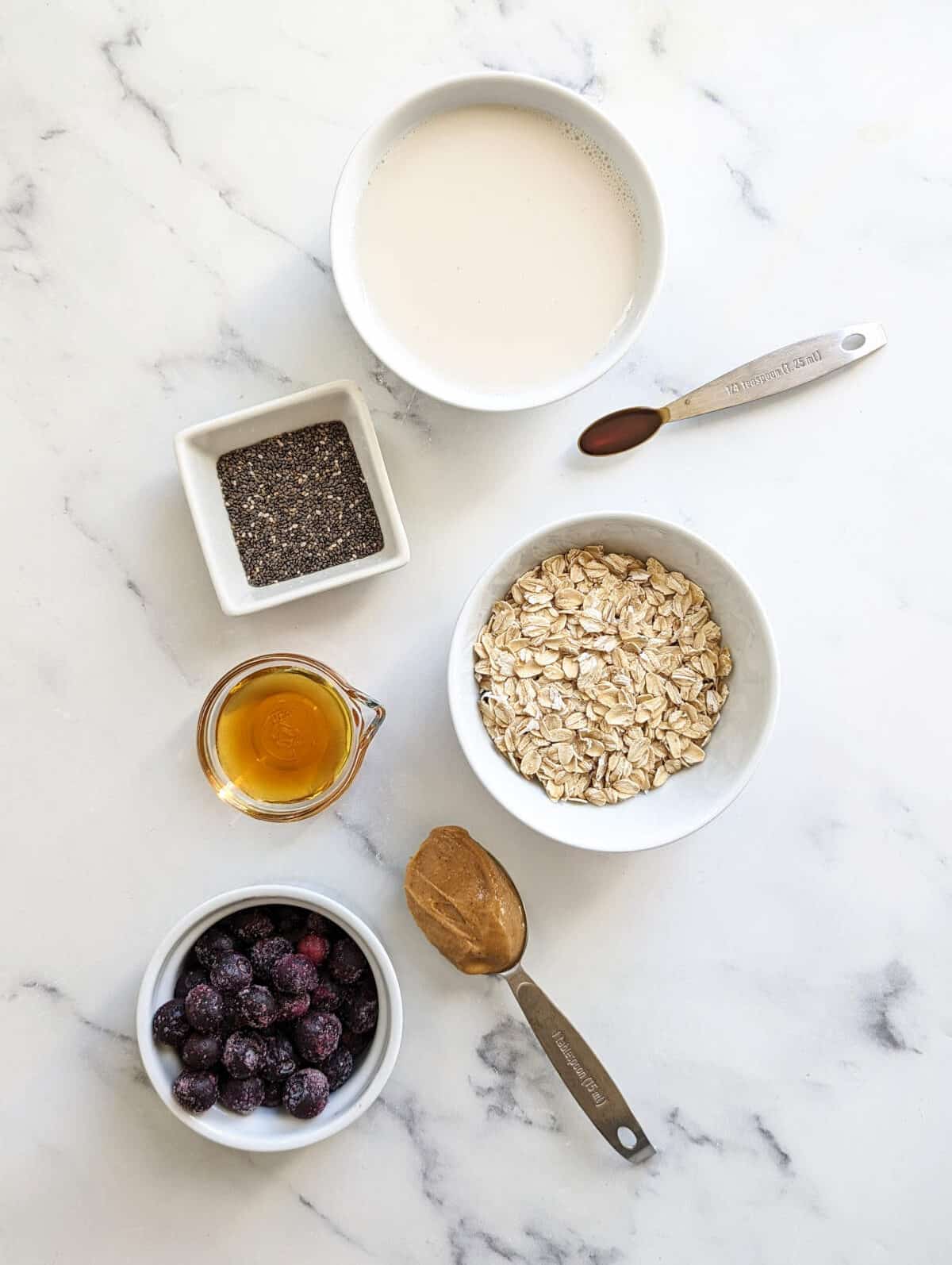 Ingredients for overnight oats with frozen fruit measured out in individual bowls and spoons.