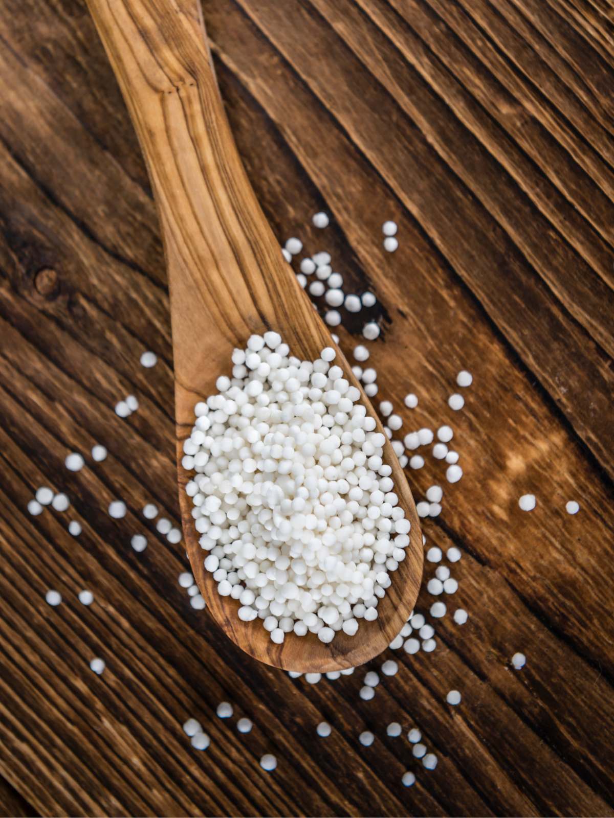 Tapioca pearls on a wooden spoon sitting on a wooden table with some tapioca balls spilling on it.