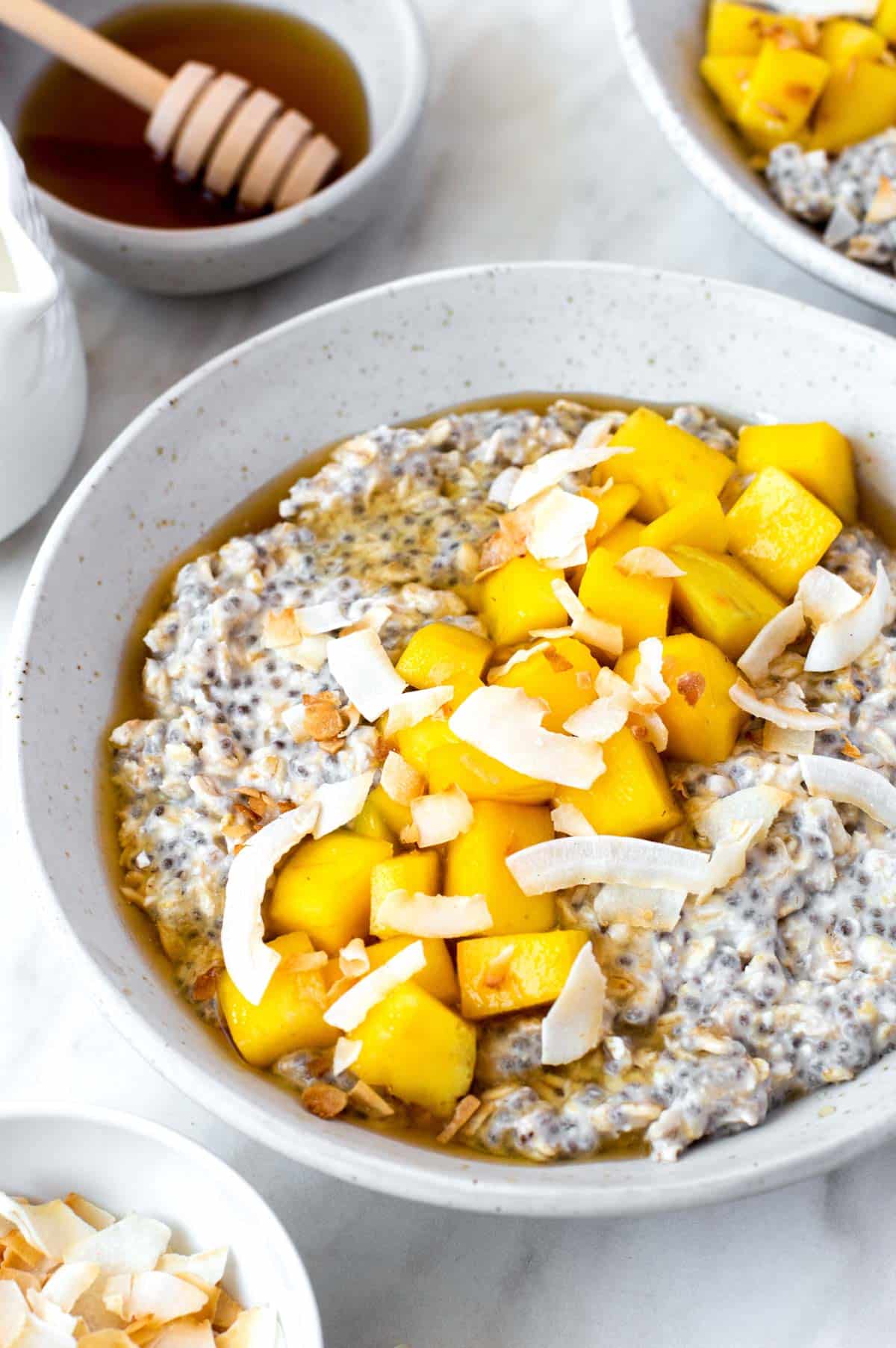 A white bowl filled with overnight oats and topped with mango and toasted coconut flakes.