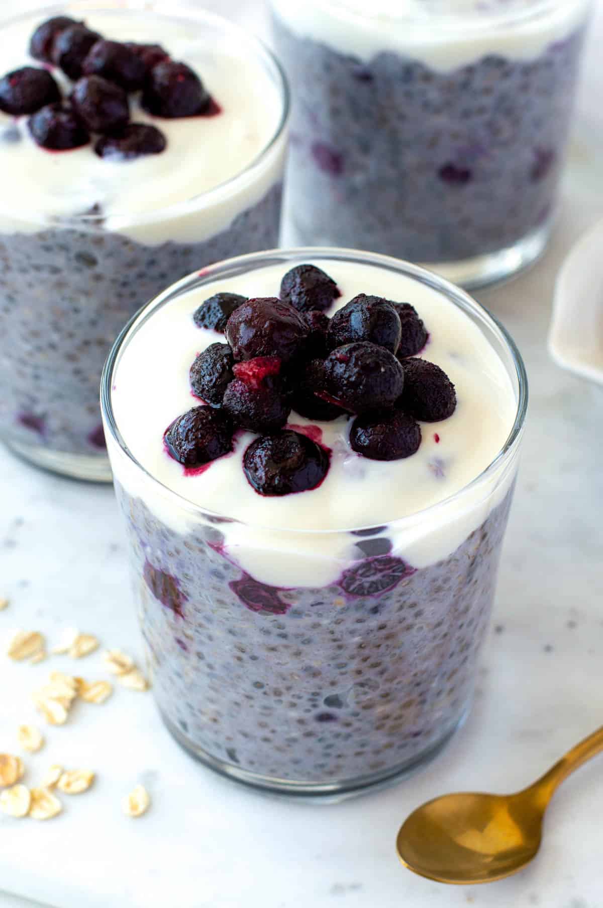 Three glass cups filled with overnight oats with frozen fruit, placed on a marble countertop