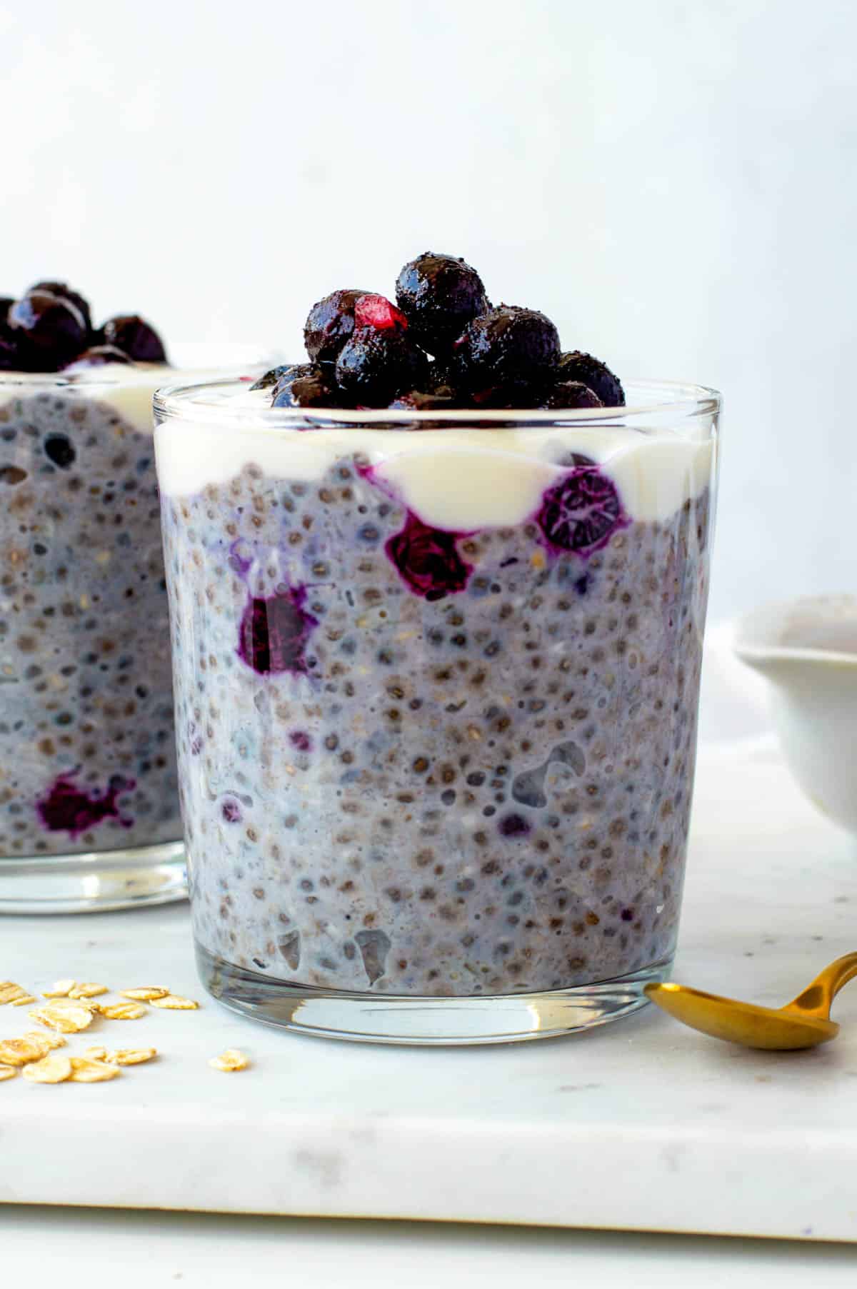 Overnight oats with frozen fruit served in a glass cup and topped with soy yogurt and frozen blueberries.