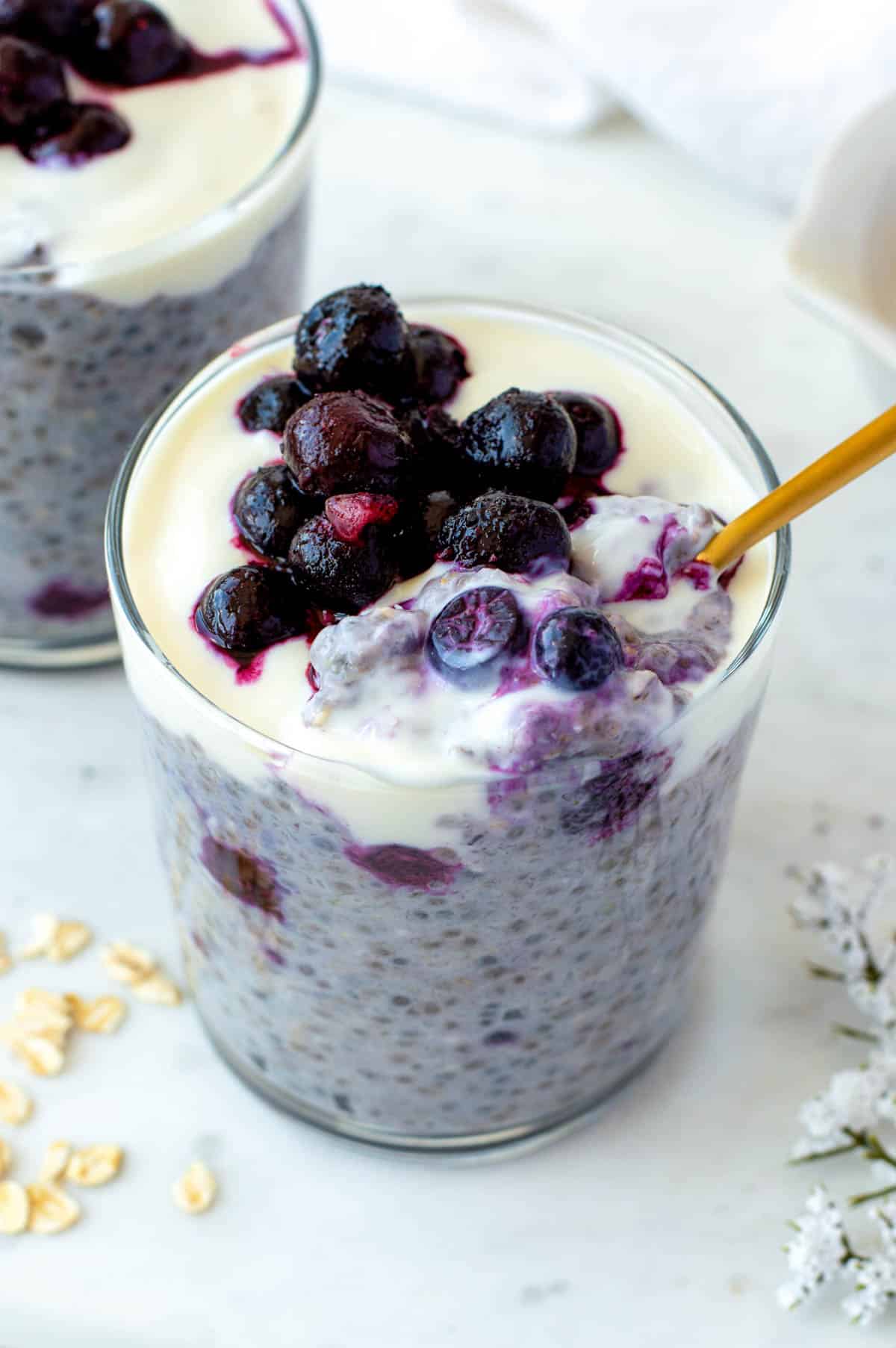 A golden spoon dipped into a glass cup filled with overnight oats with frozen fruit.