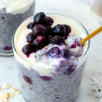 A golden spoon dipped into a glass cup filled with overnight oats with frozen fruit.