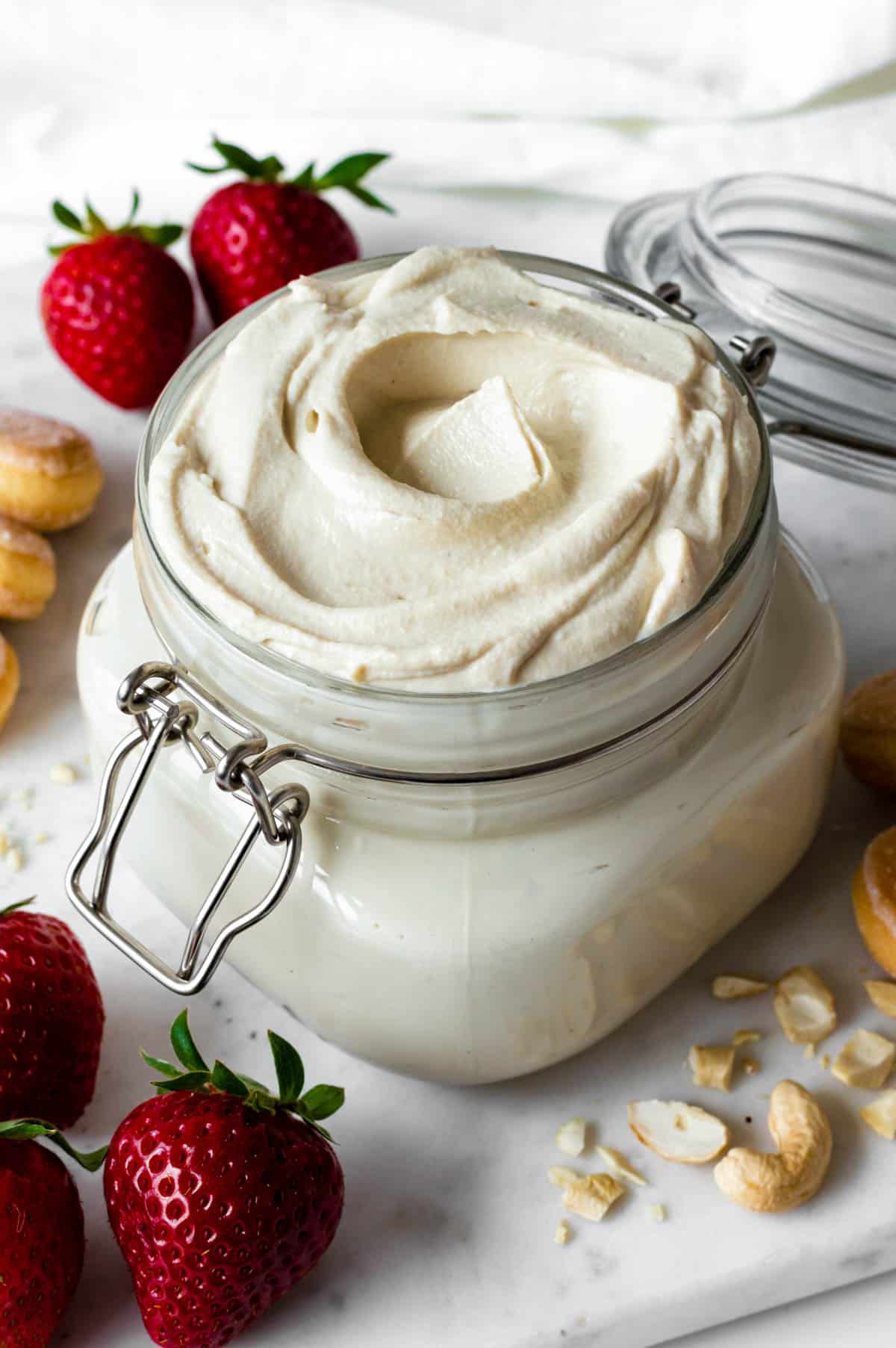 Vegan mascarpone served in a jar, placed next to strawberries, crushed cashews, and ladyfingers.